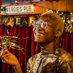 Satchel Williams, a young Black actor with cropped blonde hair is smiling, holding a piece of gold tinsel